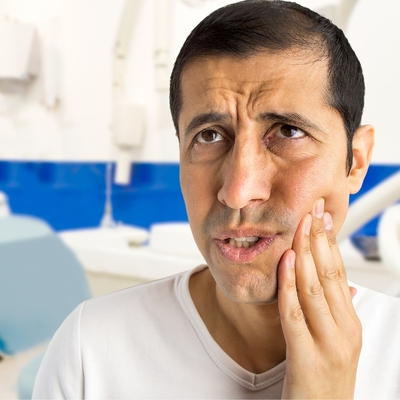 man holds the side of his jaw and winces with anticipation of a dentist visit